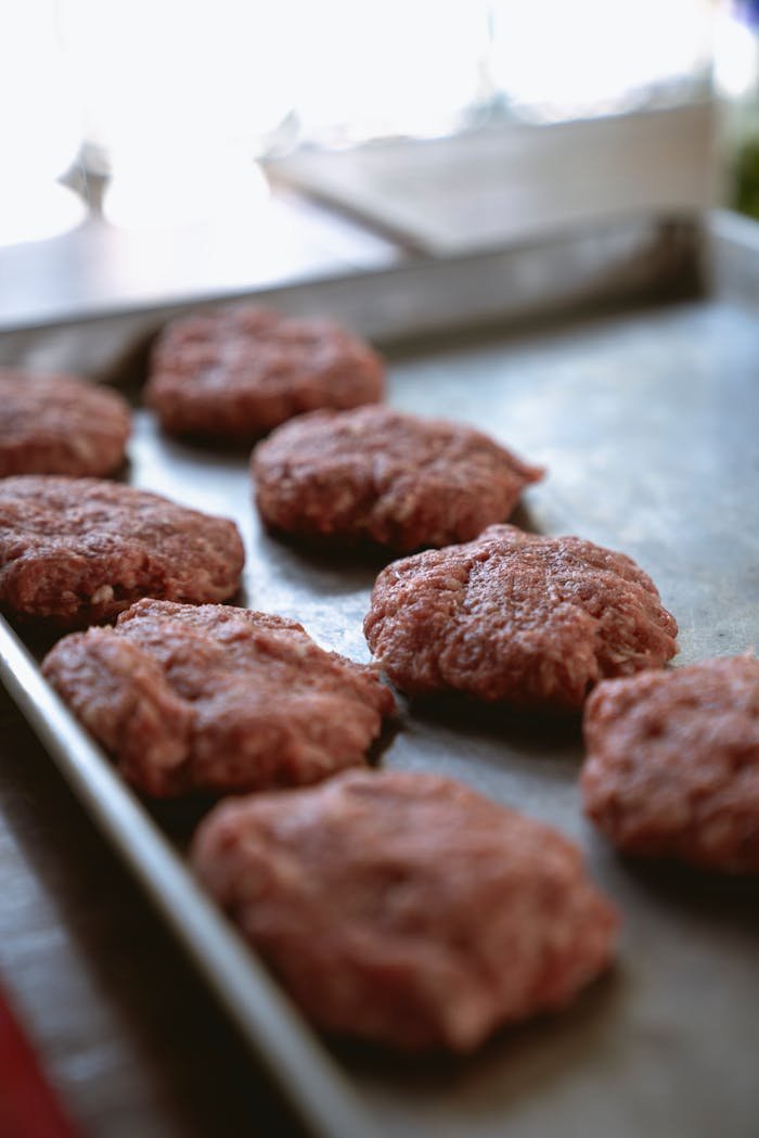 Close-up of raw beef patties on a metal tray ready for cooking.