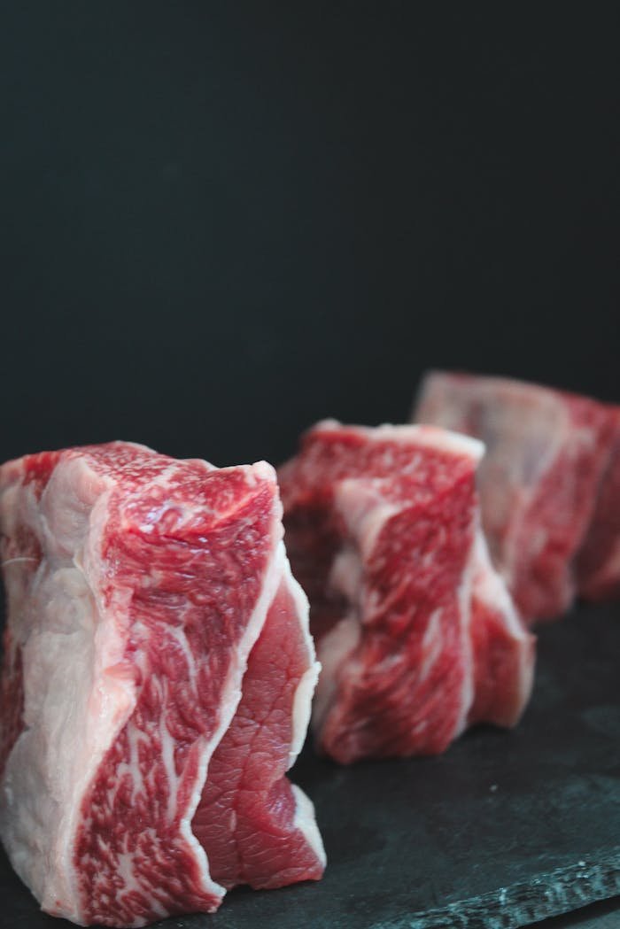Close-up of raw beef cuts with marbling on a dark surface ready for cooking.